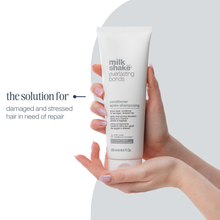 Load image into Gallery viewer, Hand holding a tube of 'milk_shake' conditioner with text about hair care on a white background