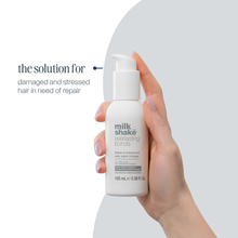 Load image into Gallery viewer, Hand holding a bottle of 'milk shake' hair treatment with text on a white background