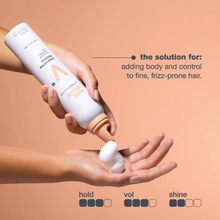 Load image into Gallery viewer, Hand holding a bottle of milk_shake volumizing mousse with text on a beige background