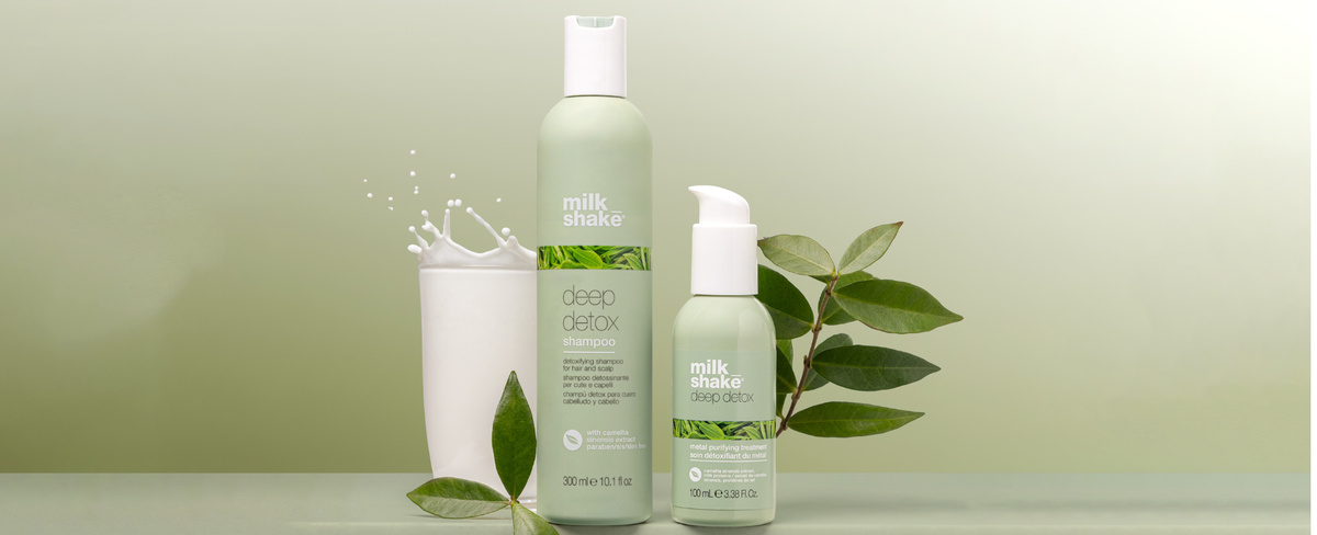 Two bottles of milk_shake deep detox shampoo and metal purifying treatment with green leaves on a light green background