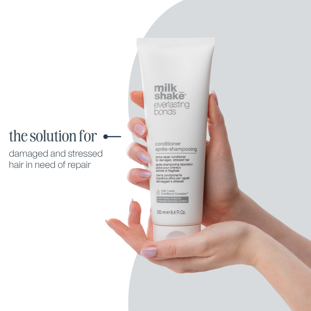 Hand holding a tube of 'milk_shake' conditioner with text about hair care on a white background